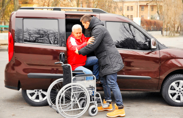 man helping elderly man in wheelchair get in the car